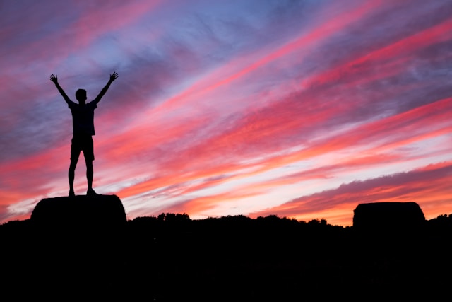 Hombre levantando los brazos en un atardecer en la cima de una montaña