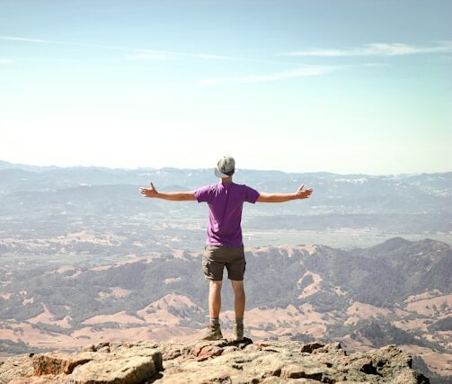 Hombre de espaldas con los brazos abiertos mirando el paisajes montañoso